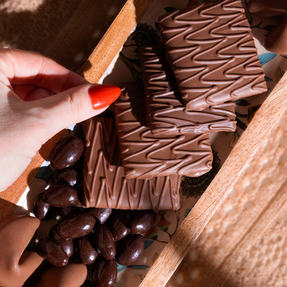 A hand reaching for Puyallup Chocolates milk chocolate covered graham crackers on a charcuterie board with dark chocolate covered almonds and milk chocolate covered fortune cookies.